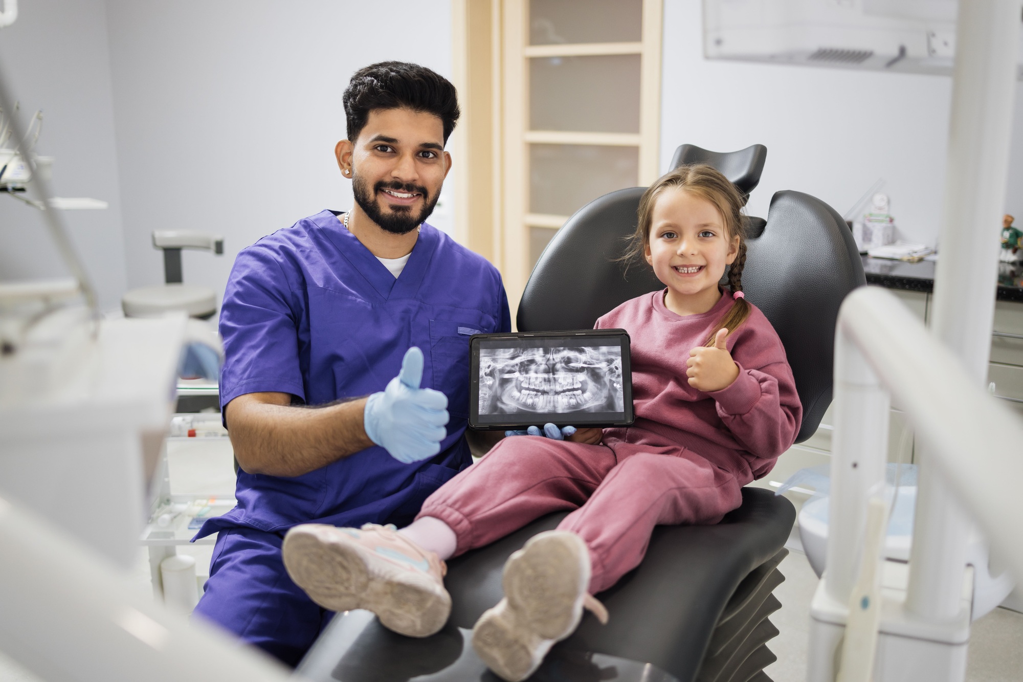 Caucasian preschool girl, sitting on dentist chair and looking at digital tablet with x-ray scan