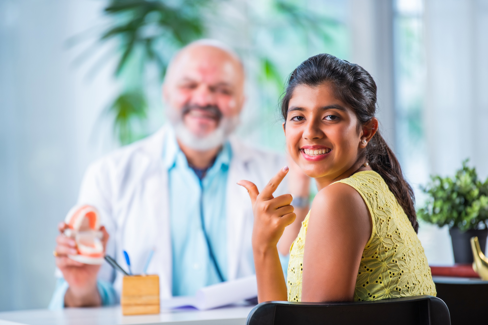 Elderly, senior or old male Indian asian dentist with girl child patient in clinic