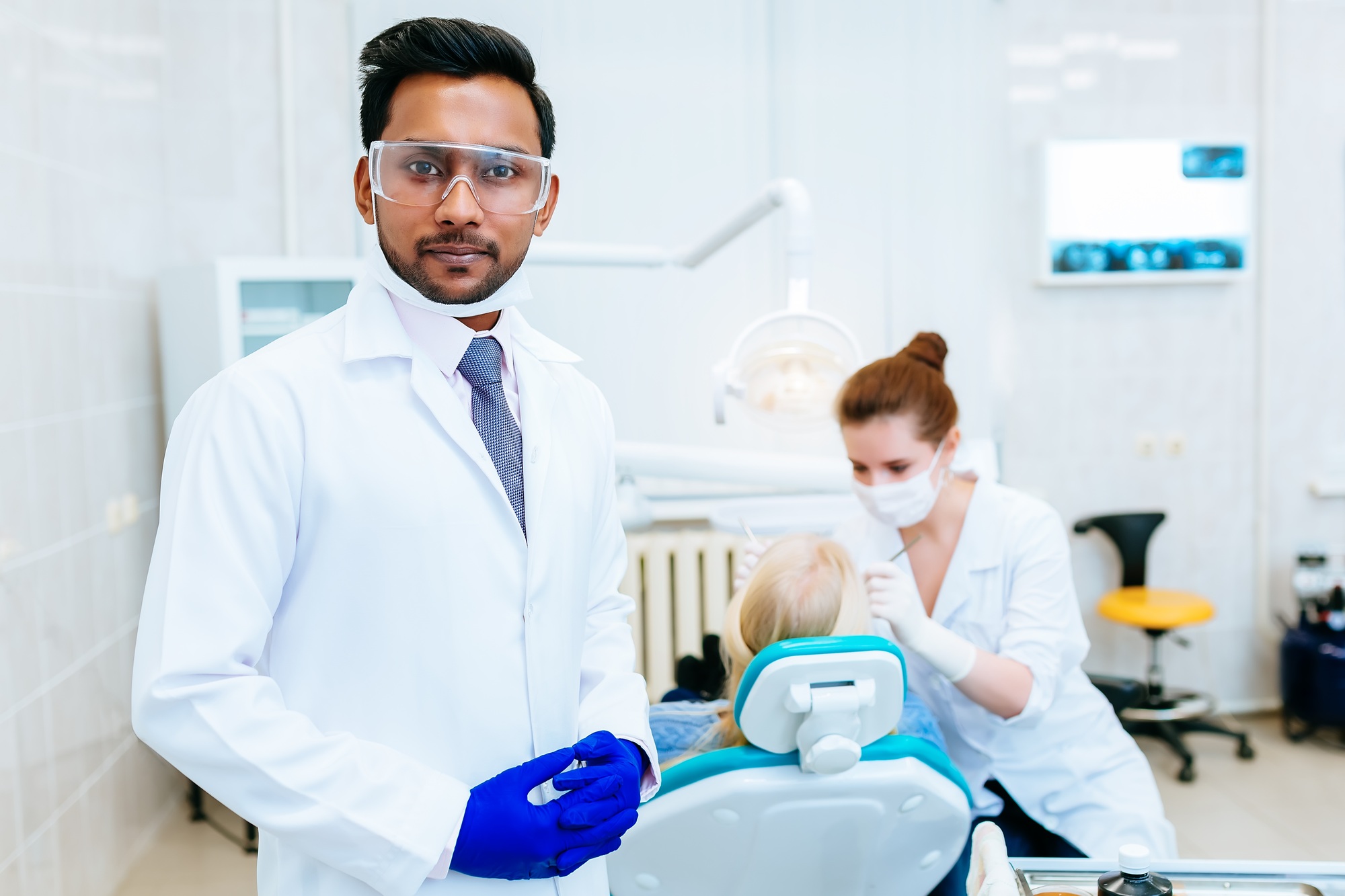 Portrait of a young confident asian male dentist in clinic in front of female dentist checking teeth